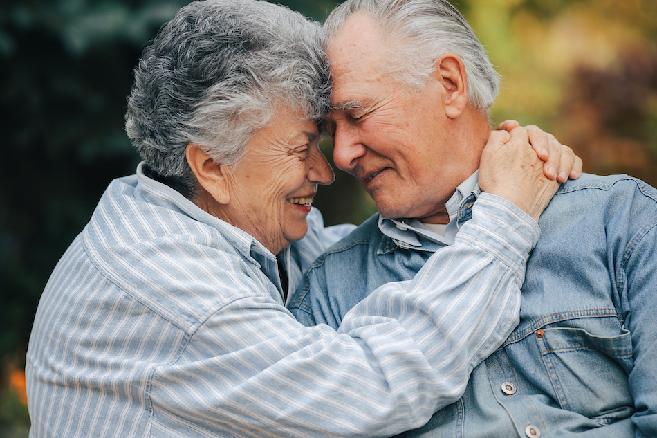 Old couple in a park. Grandparents embracing. Woman in a blue shirt.